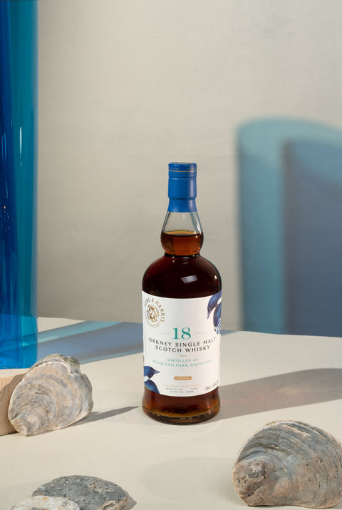 A bottle of Ferg and Harris 18-year-old Highland Park, with seashells next to it and blue transparency and shadow in the background