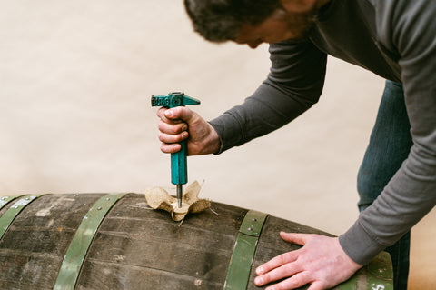 A male figure using a bung puller to open a barrel