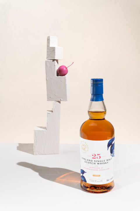 A bottle of the Ferg and Harris 25-year-old Auchentoshan next to a step like sculpture with a mini pink apple on top