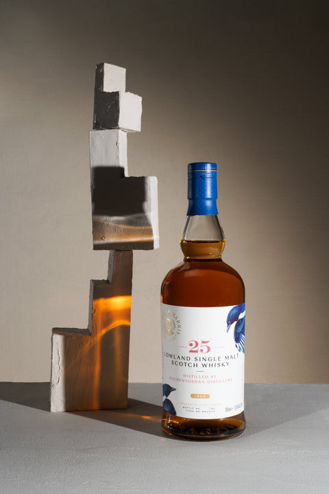 A bottle of Ferg and Harris 25-year-old Auchentoshan, with a stair like ceramic sculpture on a side a bright amber light shining on it