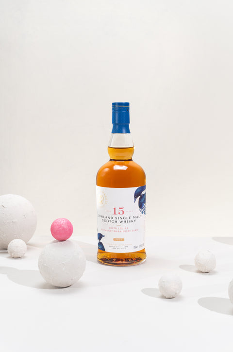A bottle of Ferg and Harris 15-year-old Auchentoshan in a white background, surrounded by 5 white spheres and one pink 