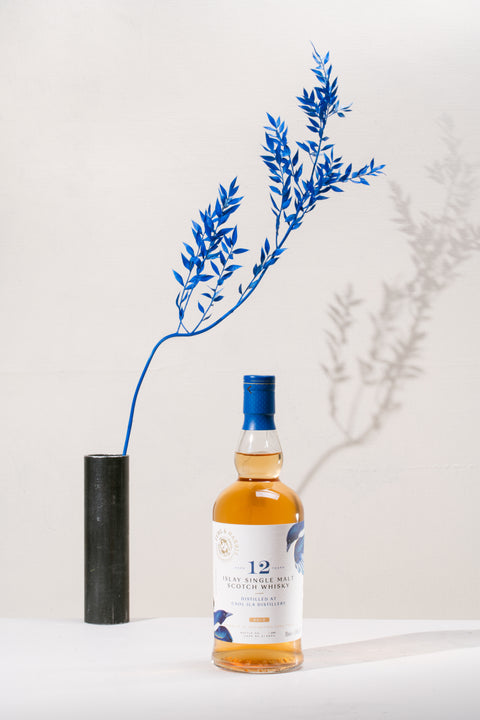 A bottle of Ferg and Harris 12-year-old Caol Ila, with a black vase with royal blue dried branch in the background